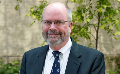 Jim outdoors, smiling, wearing glasses and suit and tie