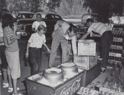 People at a picnic reaching into Coca-Cola coolers filled with ice